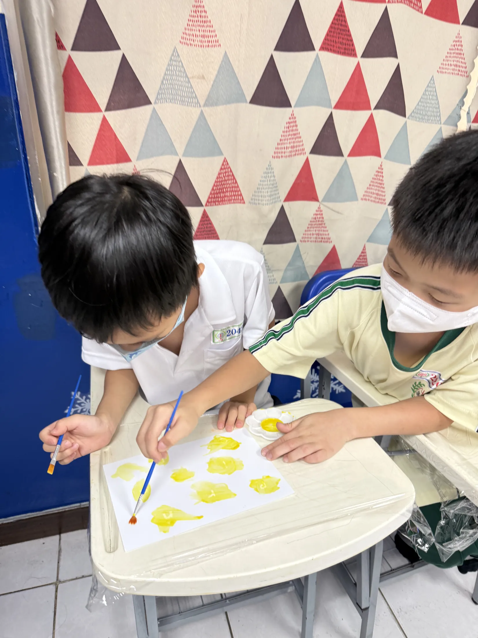 Color Lab 課堂上，兩個孩子低頭用黃色顏料畫圓點